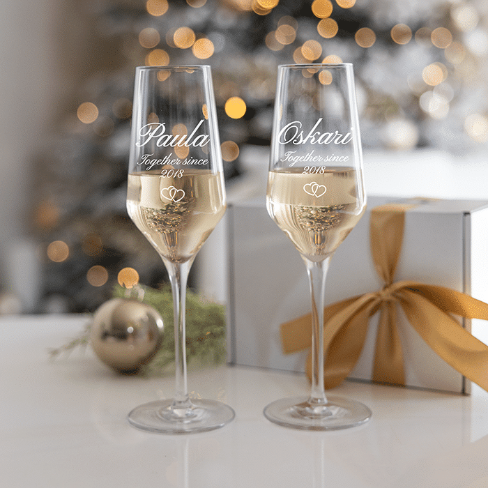 Zwei wunderschöne Sektgläser mit Gravur zur Hochzeit, die romantisch vor einem Herz-Hintergrund anstoßen